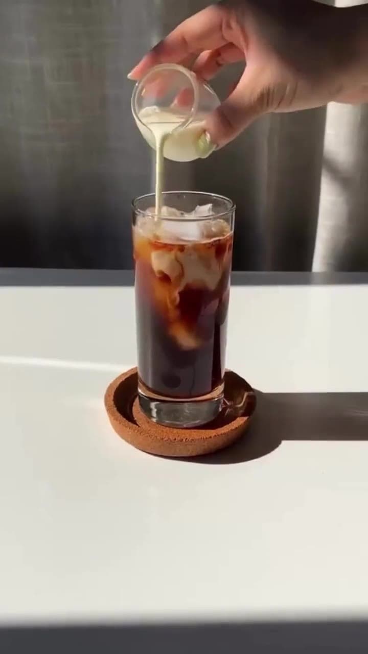 A vertical B-roll clip of milk being poured into iced cold brew